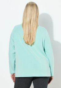 Miętowozielony, długorękawowy top wykonany z miękkiego materiału, o luźnym fasonie i okrągłym dekolcie, zestawiony z ciemnoszarymi legginsami.