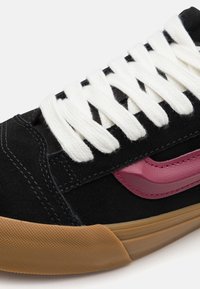 Baskets en daim noir avec lacets blancs, accent en cuir rose et semelle en caoutchouc gomme texturée. Présente des détails brodés le long des bords.