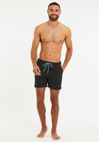 Bañador negro con cintura elástica y cordón turquesa, con bolsillos laterales y una textura de tela suave.