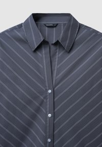 Camicia grigia con colletto, caratterizzata da righe verticali bianche, con chiusura frontale a bottoni e tessuto dalla texture liscia. Etichetta del marchio "CALLIOPE" visibile.