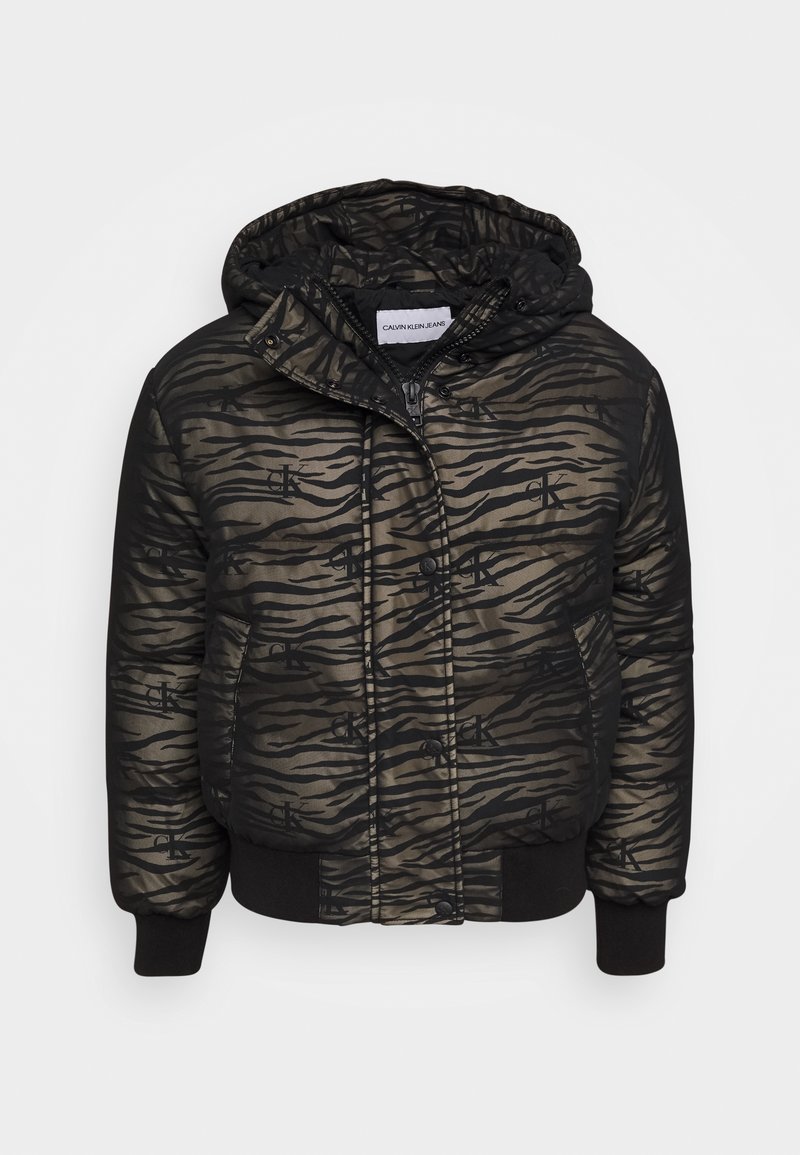 Vadderad huvmössa i svart och olivgrön, med tigerstripe-mönster och Calvin Klein-logotyp. Ribbad mudd och fåll. Dragkedjestängning.