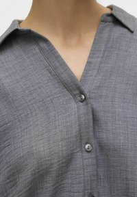 Gray button-up shirt featuring a textured fabric with a V-neck collar and subtle checks. Includes dark buttons along the front placket.