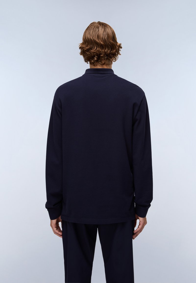 Marineblaues Langarm-Polohemd mit weicher Textur, ausgestattet mit einem klassischen Kragen und gerippten Bündchen, getragen mit passenden dunklen Hosen.