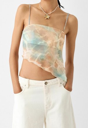 Crop top asimmetrico e trasparente in tonalità pastello di blu e pesca, con spalline sottili e una texture fluida. Abbinato a pantaloni bianchi a vita alta.