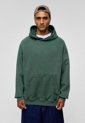 Groene oversized hoodie van een zachte katoenmix met een getextureerde zak, een capuchon met trekkoord en ribgebreide manchetten. Gepaard met denim shorts.