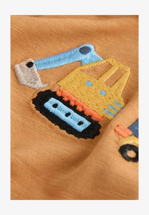 Broderad patch som föreställer ett gult byggfordon på ett mjukt, brunt tyg. Detaljer inkluderar en blå arm, orange accenter och svarta spår.