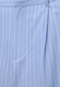 Jasnoniebieska tkanina z cienkimi białymi pionowymi kreskami, pokazująca szczegółowe przeszycia i fałdę blisko górnego prawego brzegu.