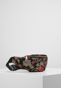 Černá vyšívaná bederní taška s květinovými vzory v červené, fialové a zlaté barvě. Obsahuje vrchní zip a nastavitelné popruhy. Hladký povrch tkaniny.