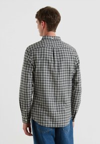 Camicia a maniche lunghe con bottoni realizzata in cotone. Presenta un motivo a scacchi bianco e nero, una vestibilità su misura e una plissettatura sul retro per facilitare i movimenti.