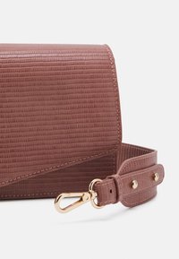 Borsa rettangolare texturizzata in rosa tenue con chiusura a patta magnetica, accessori in oro e tracolla regolabile con snap.