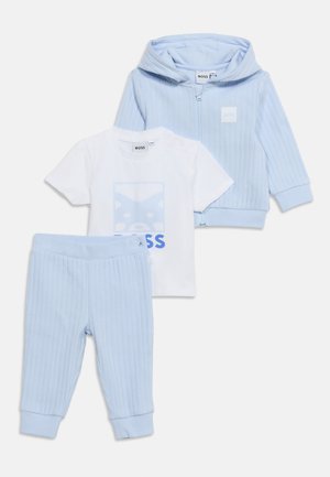 Svijetloplava rebrasta dukserica na patent i odgovarajuće hlače s bijelom majicom kratkih rukava koja ima plavi grafički motiv i tekst "BOSS".