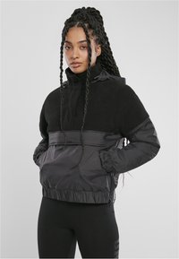 Svart tröja med dragkedja, med en mjuk fleeceöverkraft och slät nylon underdel. Har en hög krage, elastiska ärmslut och dragsko i nederkanten.