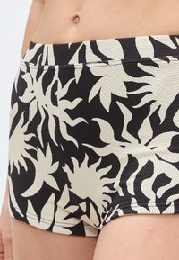 Calções de banho pretos e creme com padrão e tecido texturizado. O design apresenta formas abstratas ousadas e um ajuste justo com cintura elástica.