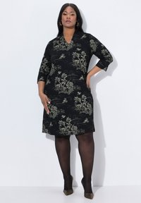 Schwarzes Kleid mit Dreiviertelärmeln, das ein florales Muster in Gold aufweist. Hergestellt aus weichem Stoff, hat es einen V-Ausschnitt und eine lockere Passform.
