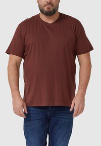 Brązowy bawełniany t-shirt z dekoltem w serek, krótkimi rękawami i luźnym krojem, zestawiony z niebieskimi dżinsami. Prosty design, bez wzorów i dodatków.