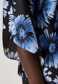 Flytende kjole med svart bakgrunn, prydet med store blå blomstermønstre. Stoffet ser glatt ut med en svak glans. Kantfinish synlig.