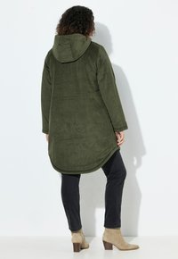 Olijfgroene corduroy lange jas met een capuchon, met een licht gebogen zoom. Gecombineerd met zwarte slim fit broeken en beige enkelbooties.