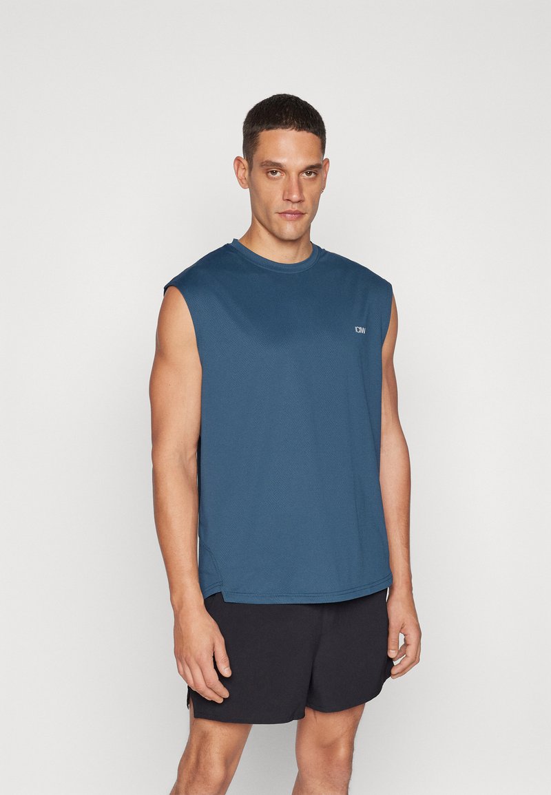 Sleeveless blue athletic shirt made of textured fabric, with a round neck and a small logo on the front. Worn with black shorts.