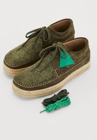Chaussures en daim vert avec un dessus texturé, semelle espadrille beige et couture marron. Comprend deux paires de lacets : noirs et verts.