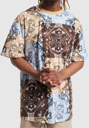 Koszulka z krótkim rękawem o wzorze patchworkowym w kolorach brązowym, beżowym i jasnoniebieskim z misternymi wzorami kwiatowymi oraz kontrastującymi czarnymi akcentami.