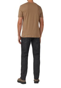 Beiges Baumwoll-T-Shirt mit kurzen Ärmeln, kombiniert mit dunkler Jeanshose. Das Outfit zeichnet sich durch einen geraden Beinverlauf und einfache Nahtdetails aus.