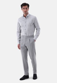 Camicia leggera grigia a fantasia con design a bottoni, abbinata a pantaloni leggeri grigi con pieghe e scarpe scure. Texture del tessuto liscia.