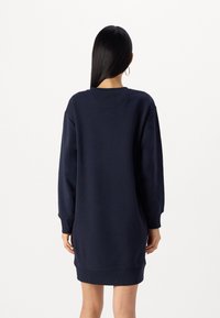 Abito felpa oversize blu navy, realizzato in tessuto morbido, con polsini e orlo a coste, colletto rotondo e spalle cadenti.