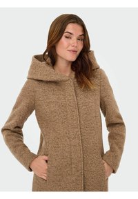 Bruine wollen mengseljas met een gestructureerde afwerking, een grote capuchon, lange mouwen en verborgen voorknoopzakken. Effen kleur zonder zichtbare patronen.