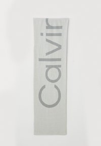 Eșarfă gri deschis cu un logo mare, stilizat "Calvin" în gri mai închis. Textură moale, cu o formă rectangulară lungă. Design simplu.