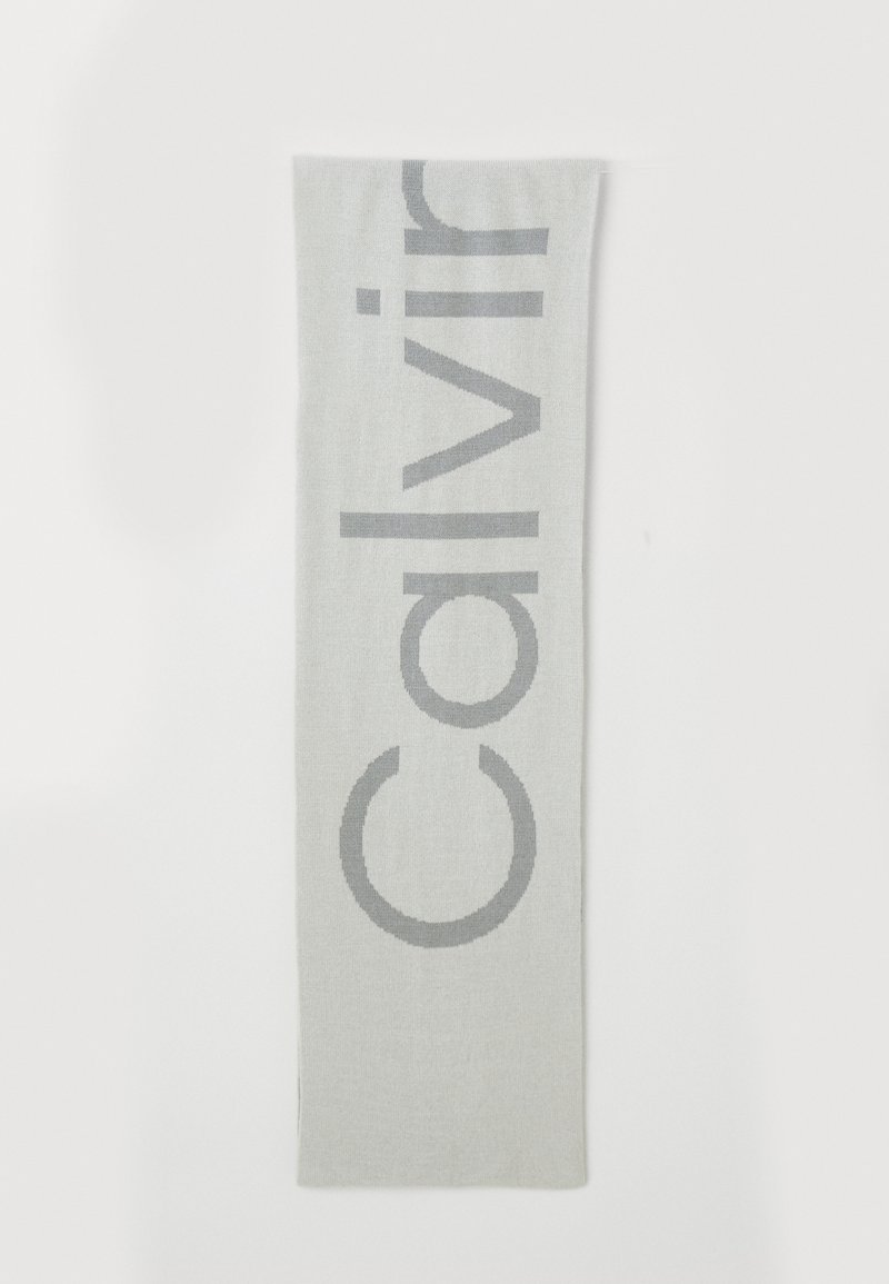 Eșarfă gri deschis cu un logo mare, stilizat "Calvin" în gri mai închis. Textură moale, cu o formă rectangulară lungă. Design simplu.