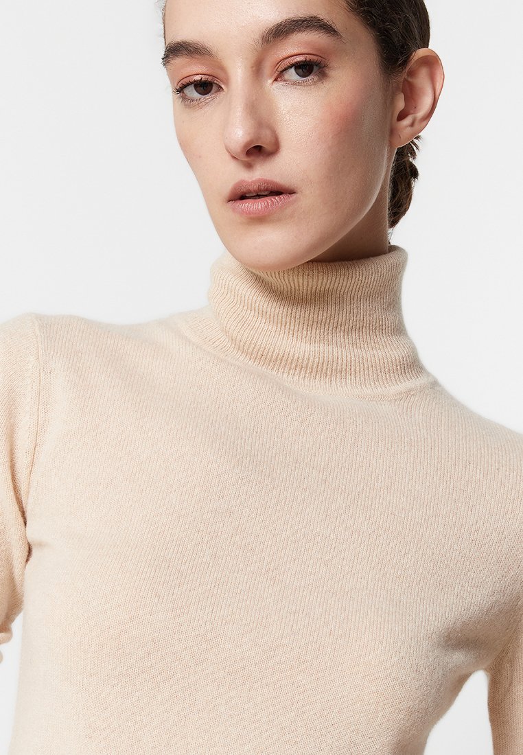 Beżowy sweter typu golf wykonanego z miękkiej dzianiny, z prążkowanym kołnierzem i dopasowanym krojem. Gładka tekstura z minimalnymi detalami.