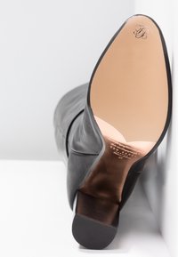 Black leather boot with a smooth texture, featuring a pointed toe and a low, chunky heel. The sole is beige, showing brand markings.