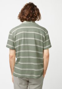 Chemise à manches courtes en vert olive, arborant des rayures horizontales blanches. Tissu doux et texturé avec une coupe décontractée.