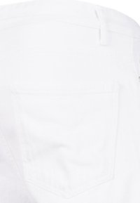 Jeans de denim blanco con un bolsillo trasero que presenta una costura diagonal. La tela parece suave con una ligera textura. No hay hardware ni adornos visibles.