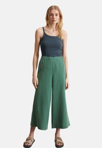 Pantaloni larghi e verdi con elastico in vita abbinati a un top aderente di colore blu navy. Il modello indossa sandali; entrambi i capi sono semplici e casual.