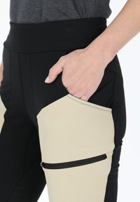 Svarta och beige träningsbyxor med hög midja, utrustade med en stor sidoficka med dragkedja och ett mjukt, elastiskt tyg.