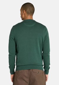 Sweter typu crewneck w ciemnozielonym kolorze z dzianiny, z ribbed rękawami i dołem, gładką teksturą oraz klasycznym krojem. Nosi się go z brązowymi spodniami.