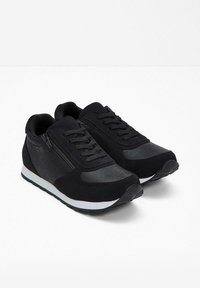 Scarpe sportive nere con un mix di materiali scamosciati e lisci, dotate di lacci e una zip laterale. Suola in gomma bianca con dettagli testurizzati.