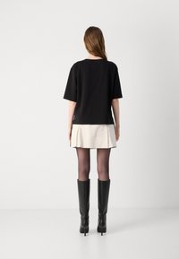Black oversized t-shirt with short sleeves, layered over a cream pleated mini skirt, paired with black knee-high heeled boots.