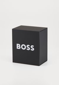Juodas kartoninis dėžė su matinio paviršiaus apdaila. Priekyje bold baltos raidės, rašančios "BOSS." Kvadratinė forma, tvarkingas dizainas, be papildomų dekoracijų.
