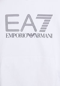 Bílá mikina s výrazným černým logem, které obsahuje "EA7" a "Emporio Armani" v různých velikostech písma, s čistými liniemi a texturovaným grafickým designem.