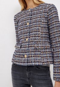 Giacca in tweed con un mix di fili blu, marroni e gialli, bottoni dorati e due tasche frontali con dettaglio frangiato all'orlo.