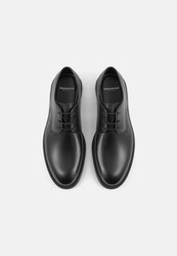 Chaussures en cuir noir avec une surface lisse, un bout rond et des lacets plats. Semelle légère avec des coutures décoratives le long du bord.