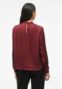 Maroon satinkbluse med en rynket halsudskæring og detalje med nøglehul bagtil, lange ærmer og sammensnørede manchetter for ekstra tekstur.