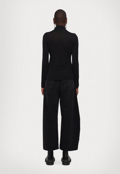 Top negru din material fluid, cu maneci lungi si guler inalt, purtat cu pantaloni cargo negri, lejeri. Design minimalist. Botine groase negre.