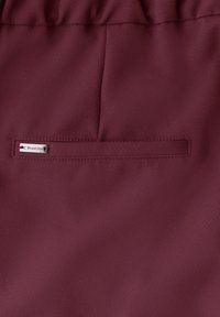 Pantalon bordeaux en tissu au toucher lisse. Dispose d'une poche cachée et d'une étiquette métallique avec le logo "Street One" sur le côté.