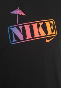 Svart t-shirt med flerfärgad "NIKE"-logotyp och en grafik av ett strandparaply ovanför texten. Mjuk tyg med en slät textur.