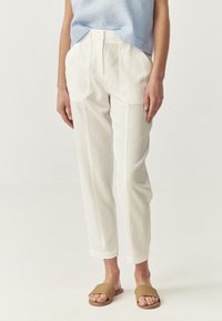 Pantaloni bianchi su misura realizzati in tessuto texture, con vita alta e tasche laterali, abbinati a sandali piatti marroni.