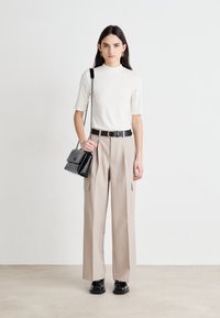 T-shirt in off-white, hoge hals, en korte mouwen; beige wijde cargobroek; zwarte riem; zwarte handtas met kettinghengsel; zwarte schoenen.