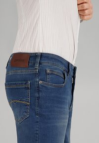 Dunkelblaue Denim-Jeans mit Slim-Fit, kontrastierenden Nähten, einem Leder-Logopatch auf der Rückseite und einem kleinen Reißverschlussfach.